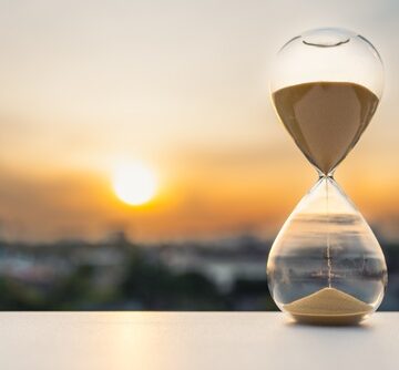 Hourglass,On,Table,At,Sunset,With,Blurred,City,Background,Symbolizing THE VANISHING VILLAGE – MEMORY, ELDERS, AND THE DEATH OF CONSEQUENCE (Part II)