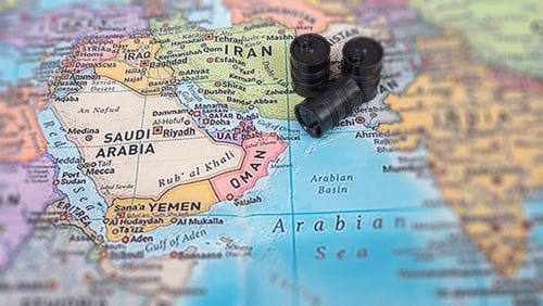 A conceptual map of the Middle East with miniature oil barrels placed over the region near the Strait of Hormuz.