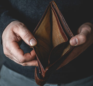 The image shows a person holding an open, empty brown leather wallet representing financial distress, poverty, or being broke. The image shows a person holding an open, empty brown leather wallet representing financial distress, poverty, or being broke.