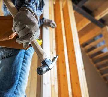 A construction worker holding a claw hammer on a wooden building construction site. A construction worker holding a claw hammer on a wooden building construction site.