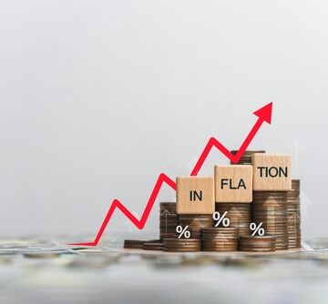Concept image of rising coin stacks and a red upward arrow over blocks spelling the word "INFLATION." Concept image of rising coin stacks and a red upward arrow over blocks spelling the word "INFLATION."