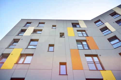 Image of the facade of a modern residential apartment building with grey paneling and colorful yellow and orange accents.