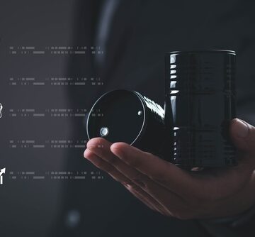 A person holding a miniature black crude oil barrel next to digital fuel and price icons. A person holding a miniature black crude oil barrel next to digital fuel and price icons.