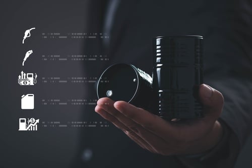 A person holding a miniature black crude oil barrel next to digital fuel and price icons. A person holding a miniature black crude oil barrel next to digital fuel and price icons.