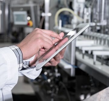 A factory worker in a lab coat uses a digital tablet to inspect an automated industrial production line. A factory worker in a lab coat uses a digital tablet to inspect an automated industrial production line.