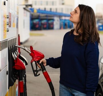 A woman holding a fuel nozzle while looking up at a gas station pump display. A woman holding a fuel nozzle while looking up at a gas station pump display.