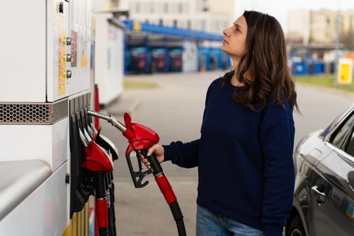 A woman holding a fuel nozzle while looking up at a gas station pump display. A woman holding a fuel nozzle while looking up at a gas station pump display.