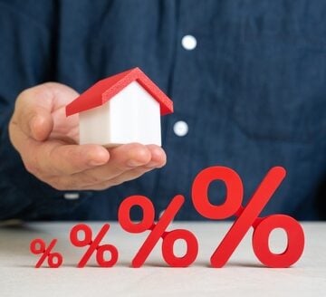 Mortgage rate concept showing a hand holding a miniature house behind increasing-sized red percentage signs. Mortgage rate concept showing a hand holding a miniature house behind increasing-sized red percentage signs.