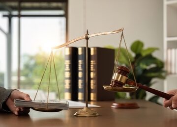 A legal consultation concept with a balance scale, law books, a gavel, and money in an office setting. A legal consultation concept with a balance scale, law books, a gavel, and money in an office setting.