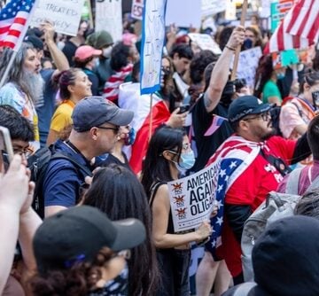 A crowd of demonstrators holding American flags and protest signs, such as one reading "America Against Oligarchy", during a nationwide "No Kings" rally. A crowd of demonstrators holding American flags and protest signs, such as one reading "America Against Oligarchy", during a nationwide "No Kings" rally.