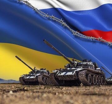 The furled national flags of Russia and Ukraine separated by a barbed wire line and with armed military tanks in the foreground. The furled national flags of Russia and Ukraine separated by a barbed wire line and with armed military tanks in the foreground.