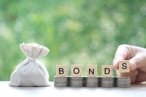 A money bag and wooden blocks spelling out "BONDS" stacked on top of coin piles. A money bag and wooden blocks spelling out "BONDS" stacked on top of coin piles.