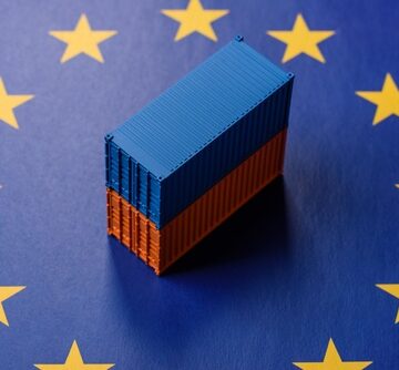 Miniature blue and orange cargo shipping containers placed on top of a blue background decorated with the yellow stars of the European Union flag. Miniature blue and orange cargo shipping containers placed on top of a blue background decorated with the yellow stars of the European Union flag.