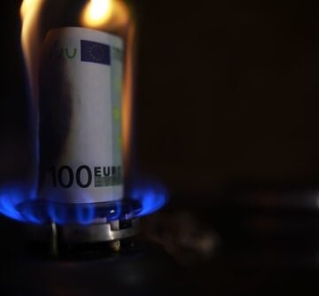 A 100-euro banknote standing upright on a lit blue gas burner, wrapped in flames to symbolize the rising cost of energy and the European gas crisis. A 100-euro banknote standing upright on a lit blue gas burner, wrapped in flames to symbolize the rising cost of energy and the European gas crisis.