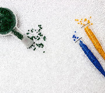 Colorful plastic polymer granules and masterbatch pellets inside a small scoop and glass test tubes used for coloring plastics.