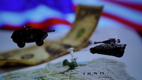 Miniature military vehicles placed over a map of Iran, with a U.S. dollar curved across the display, and a blurred American flag visible in the background. Miniature military vehicles placed over a map of Iran, with a U.S. dollar curved across the display, and a blurred American flag visible in the background.