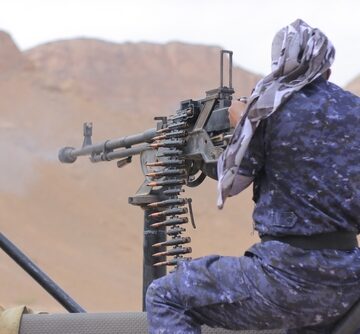 The image shows a Houthi fighter operating a heavy machine gun mounted on a vehicle in Yemen.