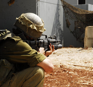 An Israeli infantry soldier taking a kneeling or crouching position while holding a rifle with an attached grenade launcher during an urban training exercise or drill. An Israeli infantry soldier taking a kneeling or crouching position while holding a rifle with an attached grenade launcher during an urban training exercise or drill.