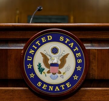 The official seal of the United States Senate mounted on a wooden dais or podium. The official seal of the United States Senate mounted on a wooden dais or podium.