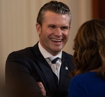 A laughing Secretary of Defense Pete Hegseth in conversation with a woman.