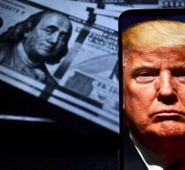 A smartphone displaying a portrait of U.S. President Donald Trump against a background of stacked U.S. 100-dollar bills featuring Benjamin Franklin. A smartphone displaying a portrait of U.S. President Donald Trump against a background of stacked U.S. 100-dollar bills featuring Benjamin Franklin.