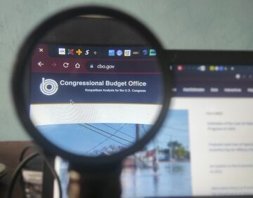 A person using a magnifying glass to view the official website of the Congressional Budget Office (CBO) (cbo.gov) on a computer screen. A person using a magnifying glass to view the official website of the Congressional Budget Office (CBO) (cbo.gov) on a computer screen.