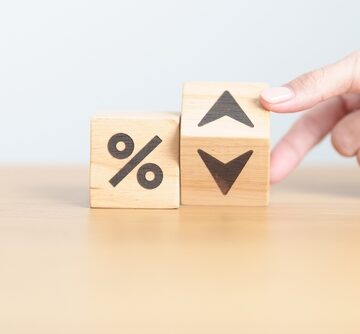 A hand turning over one of two wooden blocks featuring a percent symbol and directional arrows. A hand turning over one of two wooden blocks featuring a percent symbol and directional arrows.