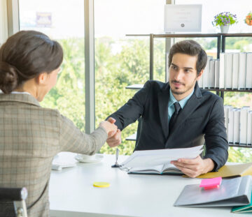 A professional business meeting or job interview setting where two people are shaking hands across a desk.