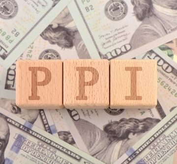 A table strewn with U.S. $100 bills is topped by three wooden blocks with the letters "PPI" standing for Producer Price Index. A table strewn with U.S. $100 bills is topped by three wooden blocks with the letters "PPI" standing for Producer Price Index.