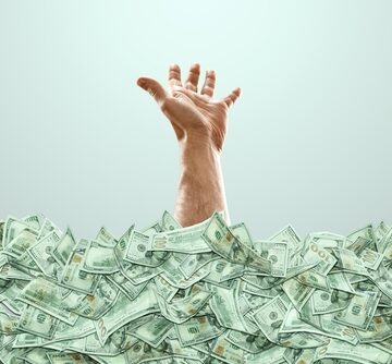 A human hand sticks out of a pile of money as if "drowning" in wealth. A human hand sticks out of a pile of money as if "drowning" in wealth.