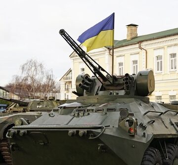 A Ukrainian armored personnel carrier (resembling a BTR-3 or similar wheeled combat vehicle) mounted with an autocannon turret and flying the Ukrainian flag.