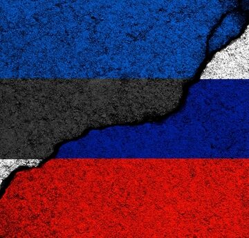 Conceptual illustration of the Estonian flag on the left and the Russian flag on the right, separated by a jagged crack across a concrete wall background.