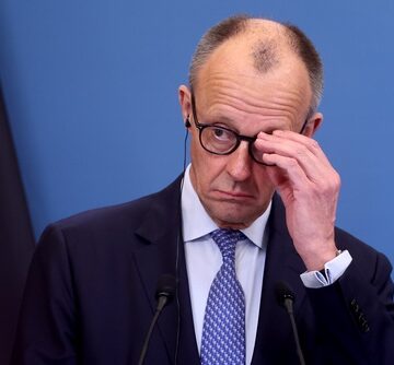 German Chancellor Friedrich Merz adjusting his glasses during a press conference.