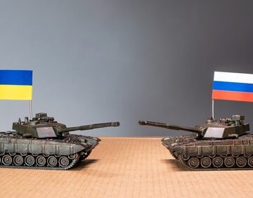 Two model toy tanks facing each other, featuring the Ukrainian flag on the left and the Russian flag on the right.