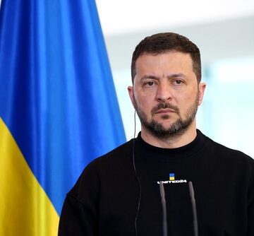 Ukrainian President Volodymyr Zelenskyy standing in front of a Ukrainian flag.